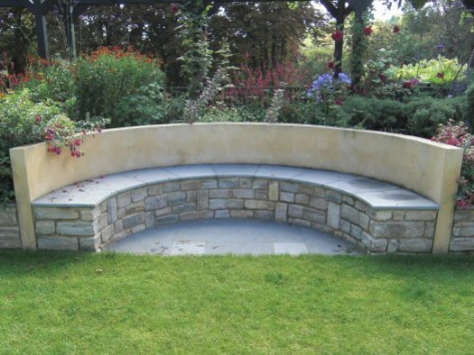 Large sloping garden design in Kenley, Surrey with stone faced retaining walls and semi-circular built-in bench seat..